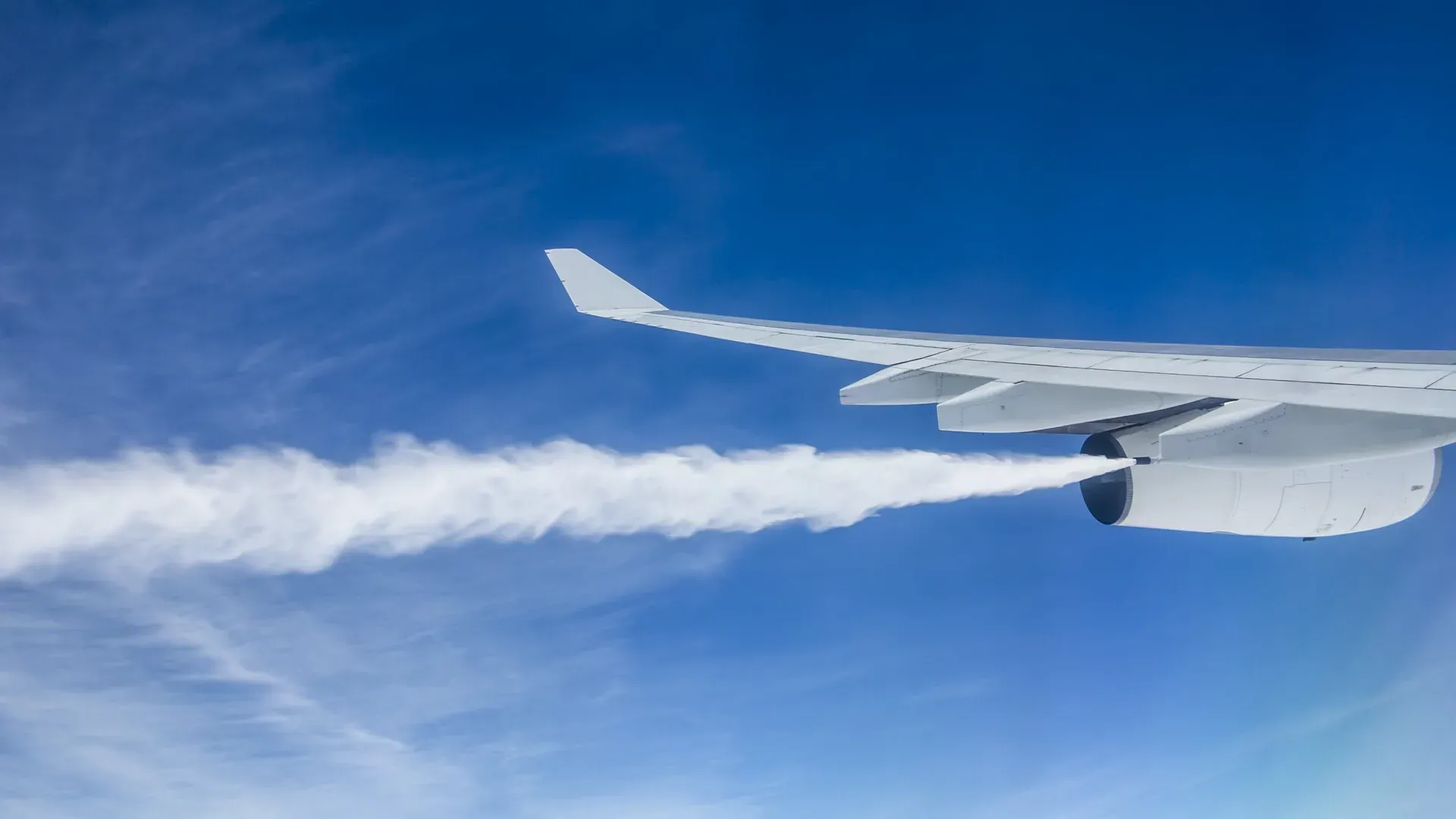A widebody airliner trailing a long plume of fuel from its wing high above the clouds